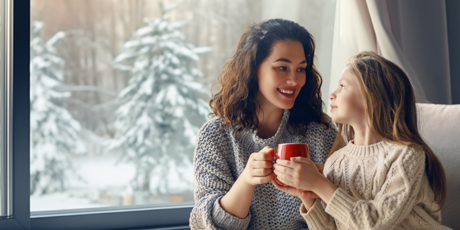 Mother and daughter drinking hot chocolate near a snowy window - AFUE 80% vs AFUE 90% Furnaces: What's the Difference?