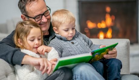 Grandfather reading book to grandchildren by fireplace
