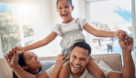 Happy family, smile and piggyback playing on sofa for quality bonding or relaxing together at home. Mother, father and child smiling for joy in playful fun and family time on the living room couch.