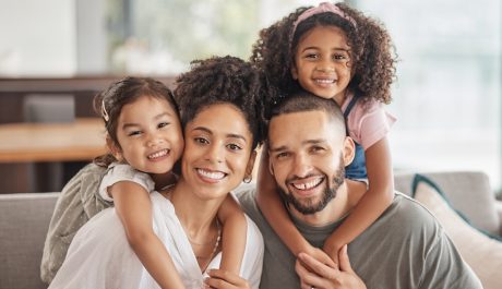 Happy, smile and portrait of an interracial family sitting on a sofa in the living room at home. Happiness, love and adoptive parents bonding, embracing and relaxing with their children in the lounge.